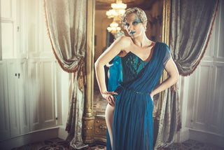 A blonde woman with bold blue makeup wears a teal corset style dress embellished with beetle shells.
